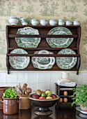 Vintage plate rack with green and white porcelain in front of floral patterned wallpaper