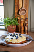 Homemade cake with cream cheese topping and blueberries on a rustic kitchen sideboard