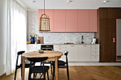 Kitchen with wall units in pink and round wooden table with black chairs