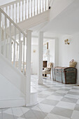 White entrance area with chequered tiled floor and antique wooden chest