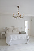 White bedroom with chandelier and wooden floorboards