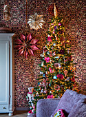 Christmas tree decorated for Christmas in front of patterned wallpaper