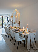 Long dining table with decoration of dried flowers, candles and ceiling lamp with fairy lights in modern dining room