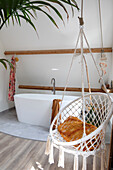 Freestanding bathtub and hanging chair in bathroom with wooden details