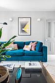 Petrol-coloured velvet couch with pink cushions in modern living room