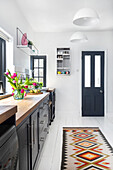 Narrow kitchen with dark cabinets, wooden worktop and colourful patterned carpet