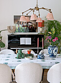 Dining table with patterned tablecloth in front of black piano, large ceiling light