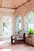 Interior with stone walls, wooden armchair with patterned cushions and potted plants