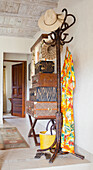 Hallway with wooden clothes rack, straw hat and patterned suitcase stack