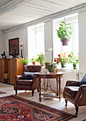 Living room with leather armchairs, round wooden table and lots of houseplants