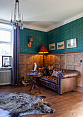 Rustic, cozy reading corner with leather sofa, wood paneling and hunting trophies