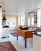 Country-style kitchen with wooden table and fruit bowl and Persian rugs on a white floor