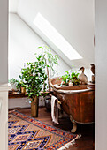 Copper bathtub with plants and oriental carpet in the bathroom under the sloping roof