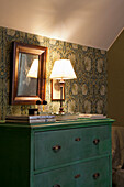 Green chest of drawers and table lamp in front of patterned wallpaper