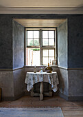 Small wooden table with flowered tablecloth in front of rustic bay window