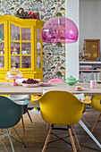 Colourful dining area with yellow display cabinet and patterned wallpaper