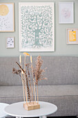 Dried flower arrangement on a round coffee table in front of a grey sofa and picture wall