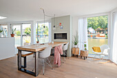 Room with wooden floor, wooden dining table, white chairs and large windows, view of river