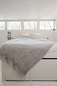 Bedroom with row of windows and light-coloured bed with grey ceiling