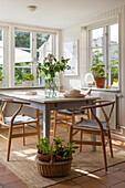 Dining area with wooden table, chairs and plants in a light-flooded room