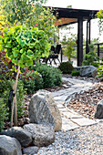 Paved garden path with stones and shrubs, terrace with wooden pergola in the background