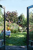 Open patio doors with view of lush summer garden with flowers and seating area