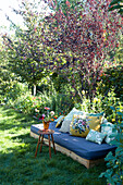 Cosy seating area with wooden sofa, mattress and colourful cushions in the summer garden