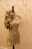 Tailor's dummy with silk fabric and feather boa in front of champagne-coloured silk wallpaper