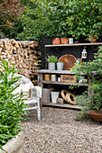 Garden workstation with shelf, herb pots and wood storage on gravel path