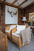 Rattan armchair with blanket and cushions in a rustic setting, antlers on the wall