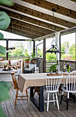 Covered wooden terrace with dining table, various chairs and seating area in the background