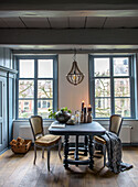 Dining area with dark wooden table, antique chairs and candlesticks in front of large windows