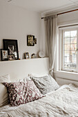 Bedroom with white bed linen and patterned pillows, with family photos on headboard