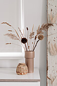 Dried flower arrangement and pompoms in a beige vase on a white table