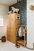 Wooden wardrobe and clothes rack in children's room with patterned wallpaper