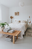 Bedroom with light-coloured bed, rattan bed bench and plant