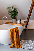 Freestanding bathtub with wooden shelf and plant, towel and carpet