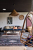 Covered terrace with sofa, rattan hanging chair and colorful rugs