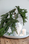 White vase with fir branches and Christmas tree ornaments on a round tray with burning candles