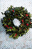 Wreath of holly branches and red berries against a mosaic tile background