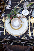 Festive table decoration with vintage porcelain cup and gold cutlery on a floral tablecloth