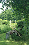 Wooden gate in the summer garden, surrounded by lush greenery and logs