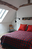 Bedroom with sloping ceiling and patchwork bedspread in blue and red