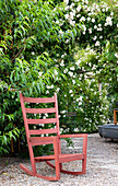 Red rocking chair on a gravelled area in front of flowering plants