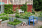 Garden benches and raised beds in front of red house with veranda