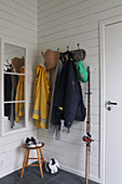 Wardrobe with jackets and fishing rod in hallway with white painted wooden panels