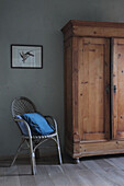 Old wooden cupboard next to rattan chair with blue pillow
