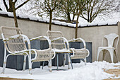 Verschneite Gartenstühle aus Rattan neben Pflanzkästen