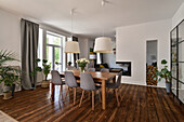 Dining area with wooden table and grey chairs, plants and fireplace in the open-plan living room