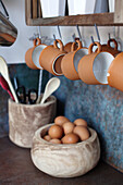 Holzschalen mit Eiern und Küchenutensilien, hängende Tassen